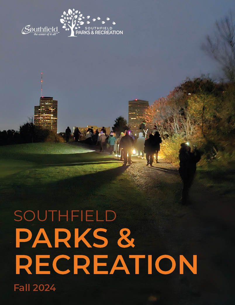 Picture of the cover of the fall activities guide featuring a picture of a group on a night hike with flashlights showing the way with two high rise buildings in the background